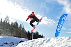 A snowboarder is jumping in the fun park during kids and adults snowboarding lessons for advanced boarders with Skischule Waidring Steinplatte.