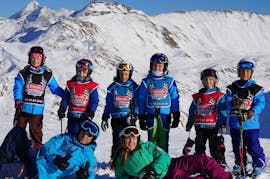 Een groep jonge skiërs poseert voor een foto op de top van de piste met hun skileraren van de skischool Snocool tijdens hun kinderskilessen "Kleine Groep" (5-12 jaar) - alle niveaus.