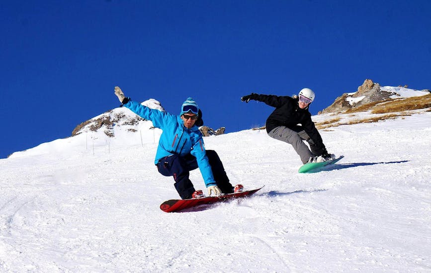 Ein Snowboarder folgt seinem Skilehrer von der Skischule SnoCool in Tignes auf einer verschneiten Piste, während er sich sein Board während des Snowboard-Privatunterrichts schnappt - Alle Levels & Altersgruppen. 
