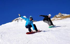 Un snowboarder sigue a su instructor de la escuela de esquí SnoCool en Tignes en una pendiente nevada, mientras agarra su tabla durante sus lecciones privadas de snowboard: todos los niveles y edades.