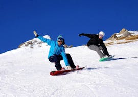 Un snowboardeur suit son moniteur de snowboard de l'école de ski Snocool à Tignes le long d'une pente enneigée tout en attrapant sa planche pendant son Cours particulier de snowboard - Tous niveaux & âges.