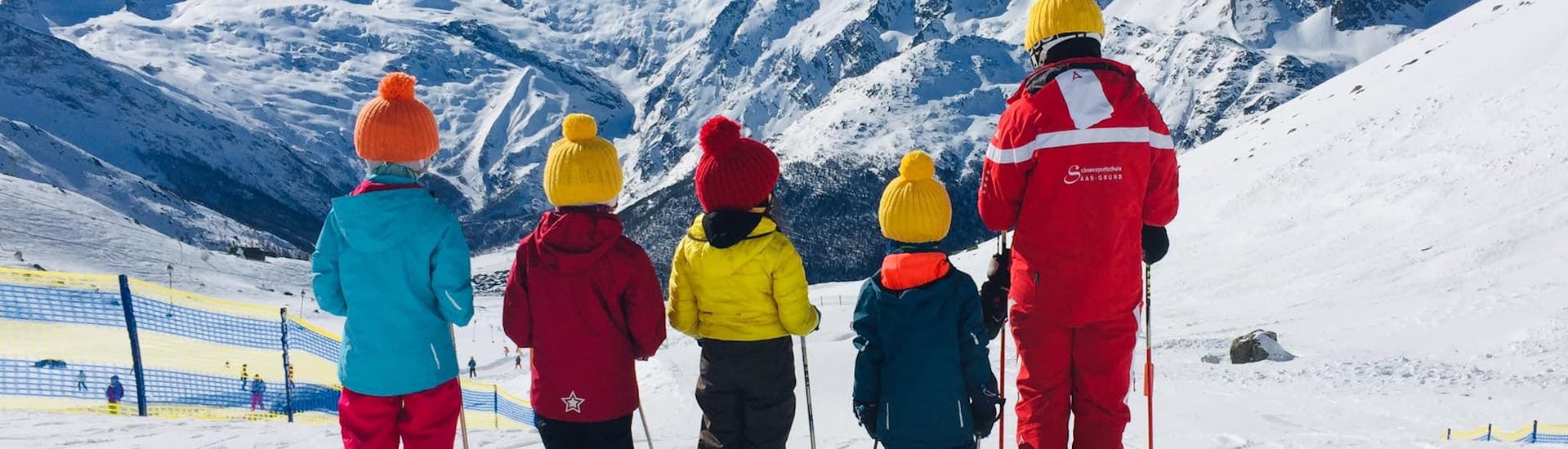 Quatre enfants et le moniteur font la queue sur la piste lors des cours de ski pour enfants (6-12 ans) pour tous les niveaux de l'école de ski suisse de Saas-Grund.