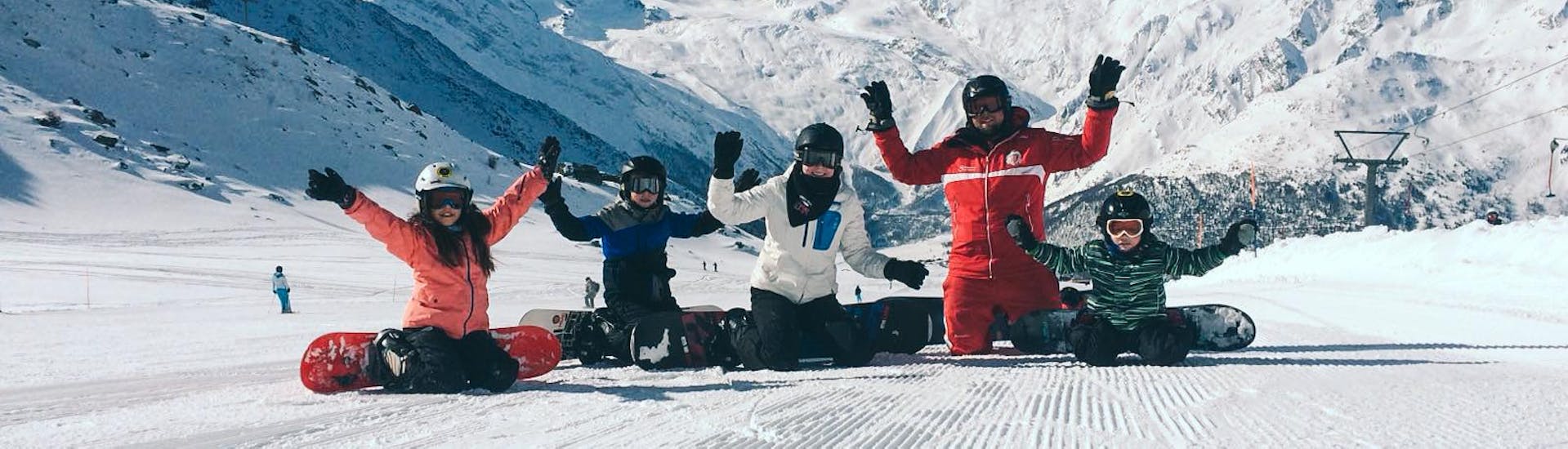 Vier snowboarders en een instructeur juichen tijdens hun Kids Snowboardingles (6-12 j.) voor beginners van de Zwitserse Skischool Saas-Grund.