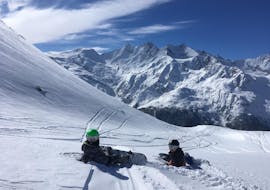 Deux snowboarders sont assis sur la piste lors des cours de snowboard pour adultes (à partir de 13 ans) pour débutants de l'école de ski suisse de Saas-Grund.