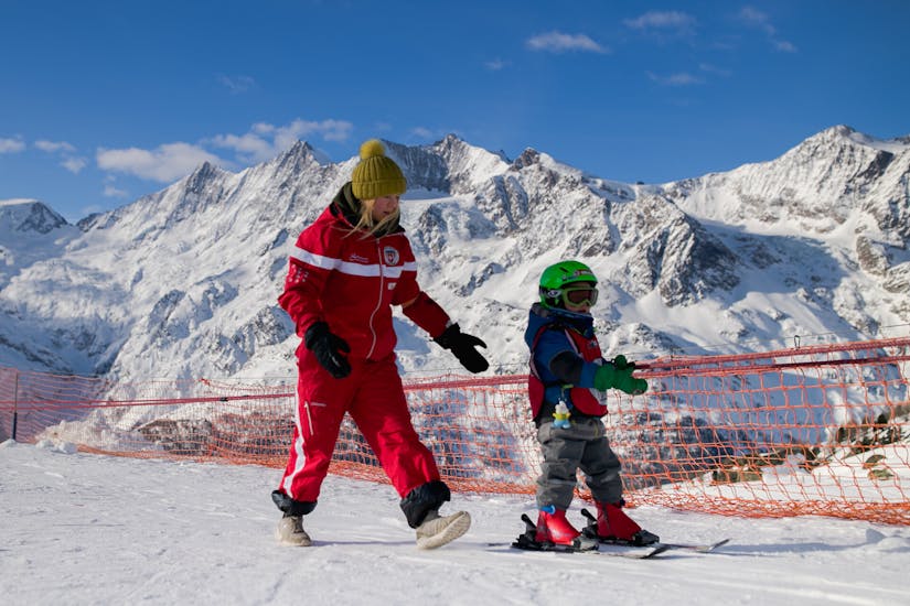 Een skileraar helpt een kind tijdens de privélessen voor kinderen van alle niveaus van de Zwitserse Skischool Saas-Grund.