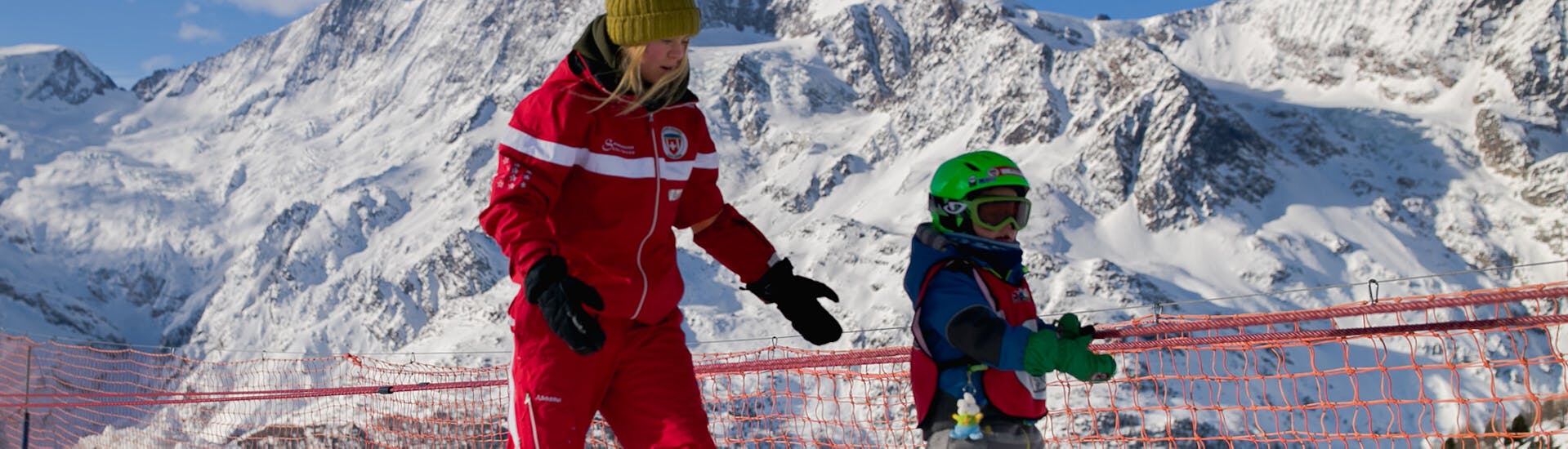 Een skileraar helpt een kind tijdens de privélessen voor kinderen van alle niveaus van de Zwitserse Skischool Saas-Grund.