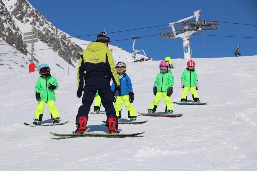 Un maestro della scuola Prosneige Val Thorens & Les Menuires insegna ai bambini sorridenti durante le lezioni di snowboard per bambini di tutte le età e di tutti i livelli.