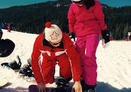 Le moniteur de snowboard aide à s'équiper lors d'un Cours particulier de snowboard (6-14 ans) pour Enfants de Tous Niveaux.