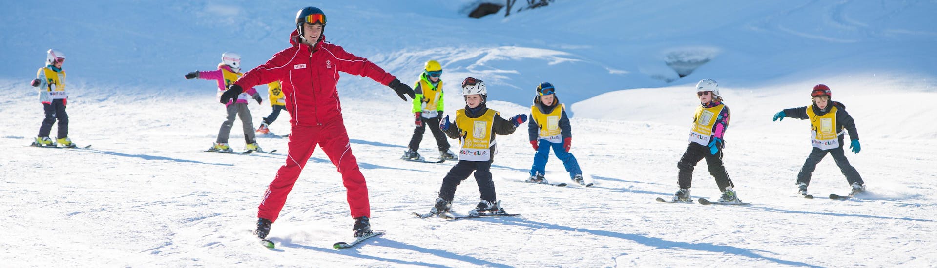 Eine Gruppe von Kindern mit ihrem Skilehrer beim Kinder-Skikurs für Anfänger der Skischule Jochberg.
