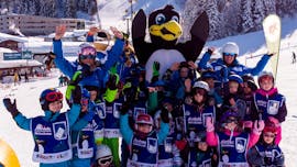 A large group of children wave to the camera together with their ski instructor during the kids ski lessons "BOBOs Miniclub" (3-4 years) - beginner of the Ski School Fieberbrunn Widmann Mountain Sports.