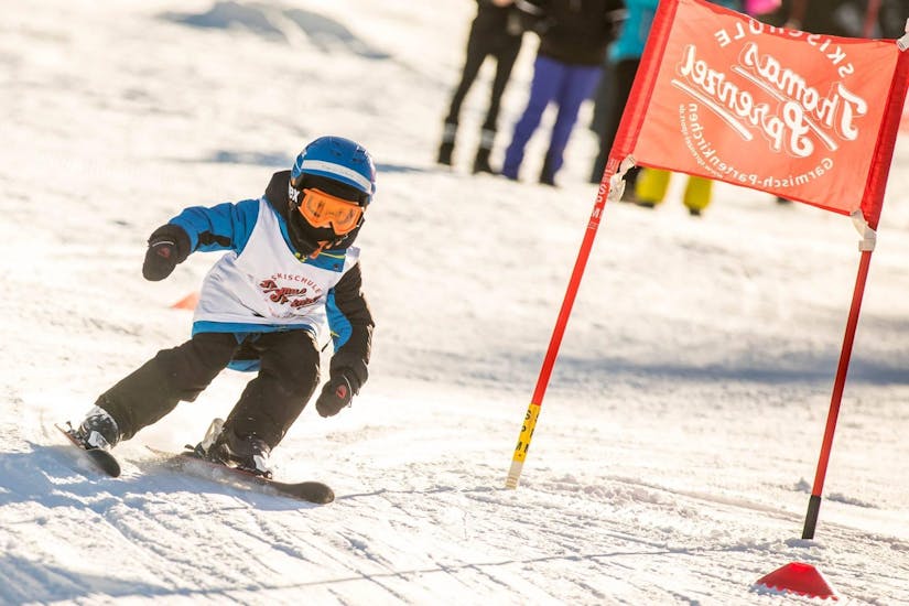 A young child is racing down a race course as part of its Kids Ski Lessons (4-12 years) - All Levels with the ski school Skischule Thomas Sprenzel in the ski resort of Garmisch-Classic.