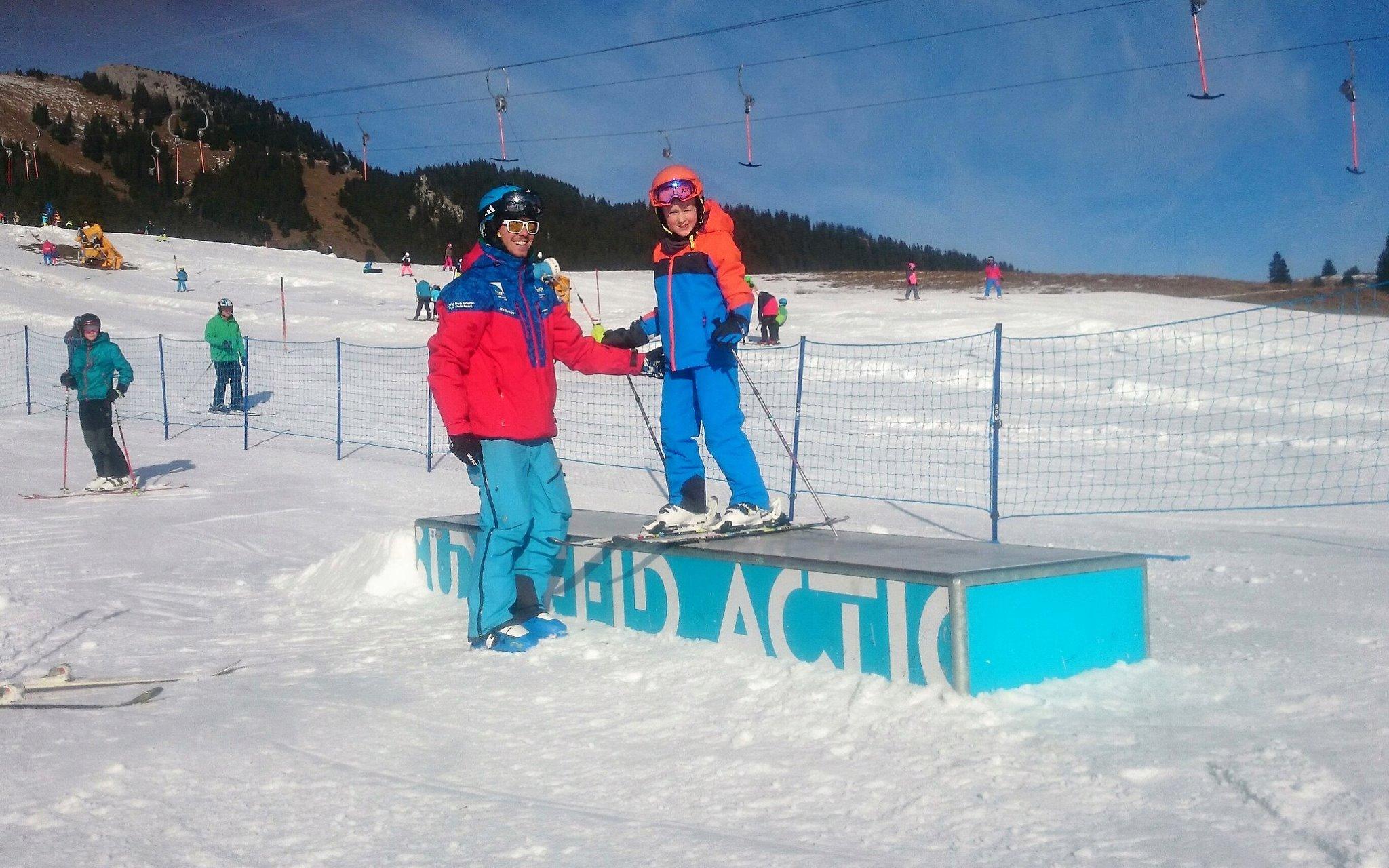 Kid standing on skiing obstacle with teacher of Alpine and Winter Sports School Top On Snow Sudelfeld