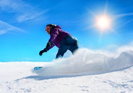 Un snowboarder prend un virage serré par une journée ensoleillée pendant ses cours particuliers de snowboard pour enfants et adultes - tous niveaux avec l'école de ski Skischule Thomas.