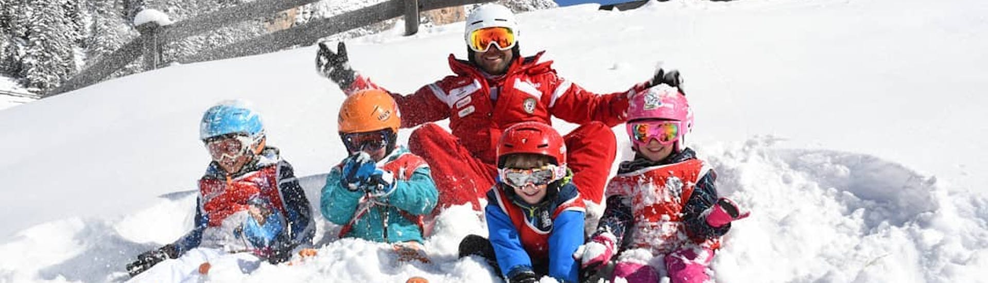 Bambini e maestro di sci si divertono sulla neve dopo una delle lezioni di sci per principianti a Selva di Val Gardena.