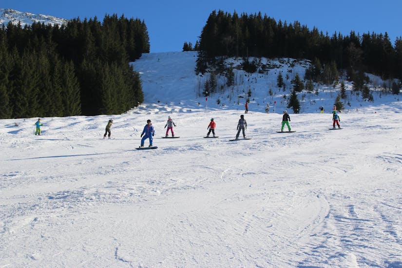 Des snowboarders sur la piste lors des cours de snowboard pour adolescents et adultes de tous niveaux de l'école de ski et de snowboard Ostrachtal.