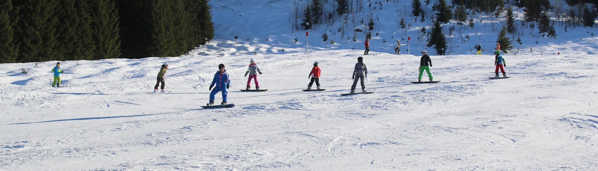 Des snowboarders sur la piste lors des cours de snowboard pour adolescents et adultes de tous niveaux de l'école de ski et de snowboard Ostrachtal.