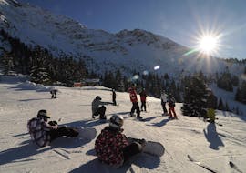 Snowboarders zitten op de piste tijdens de Kids Snowboardles (7-12 j.) voor alle niveaus van Ski & Snowboardschool Ostrachtal.