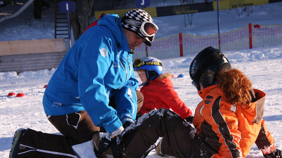 Een instructeur laat een kind zien hoe het het snowboard aantrekt tijdens privélessen snowboarden voor kinderen en volwassenen van alle niveaus van Ski & Snowboard School Ostrachtal.