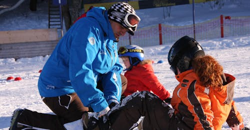 Private Snowboarding Lessons for Kids & Adults of All Levels from Ski & Snowboard School Ostrachtal An instructor showing a kid how to put on the snowboard at Private Snowboarding Lessons for Kids & Adults of All Levels from Ski & Snowboard School Ostrachtal.