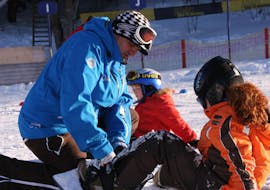 Ein Lehrer zeigt einem Kind, wie man das Snowboard anlegt, beim privaten Snowboardunterricht für Kinder und Erwachsene aller Niveaus der Ski- und Snowboardschule Ostrachtal.