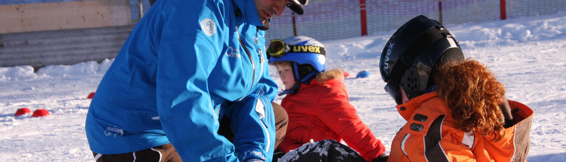 Ein Lehrer zeigt einem Kind, wie man das Snowboard anlegt, beim privaten Snowboardunterricht für Kinder und Erwachsene aller Niveaus der Ski- und Snowboardschule Ostrachtal.