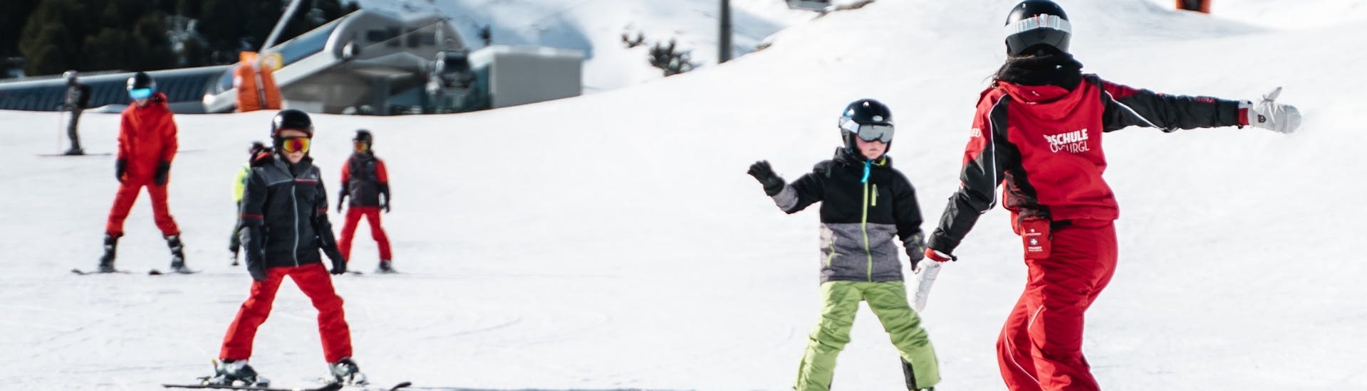 Ein Skilehrer zeigt Kindern den Weg im Kinder-Skikurs (4-16 J.) für Fortgeschrittene.