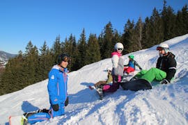 Snowboarders sentados en la pista en las clases de snowboard para niños (7-12 años) para todos los niveles de la Ski & Snowboard School Ostrachtal.