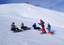 Een groep snowboarders zit in de sneeuw rondom hun snowboardleraar van de skischool Evolution 2 Tignes tijdens hun snowboardlessen voor kinderen en volwassenen.