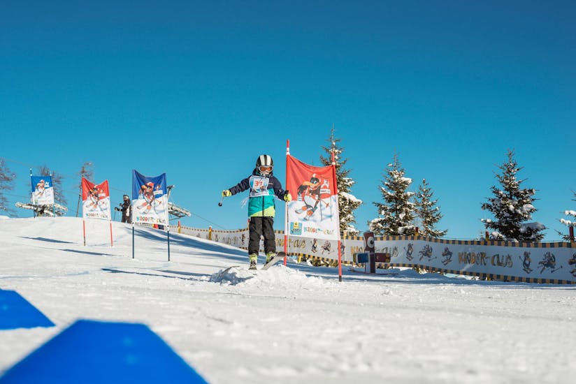 Een leerling skiet op een blauwe piste tussen de poorten tijdens zijn kinderskilessen "BOBO's Kids-Club" voor gevorderden bij de Busslehner Achenkirch Skischool.
