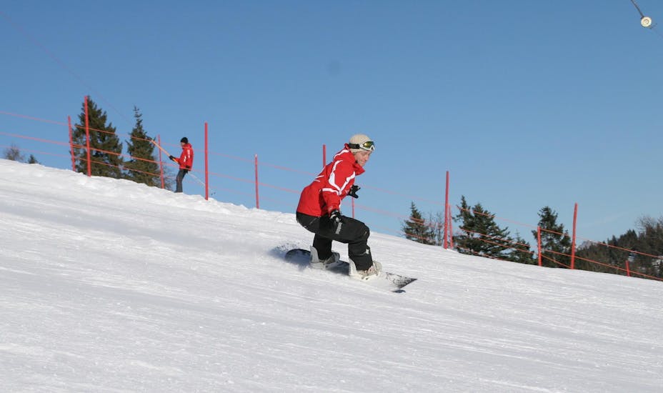 Ein Snowboarder fährt während seinem privaten Snowboardkurs für Kinder und Erwachsene aller Levels mit der Skischule Busslehner die Piste hinunter.