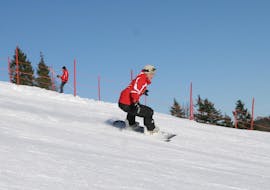 Ein Snowboarder fährt während seinem privaten Snowboardkurs für Kinder und Erwachsene aller Levels mit der Skischule Busslehner die Piste hinunter.
