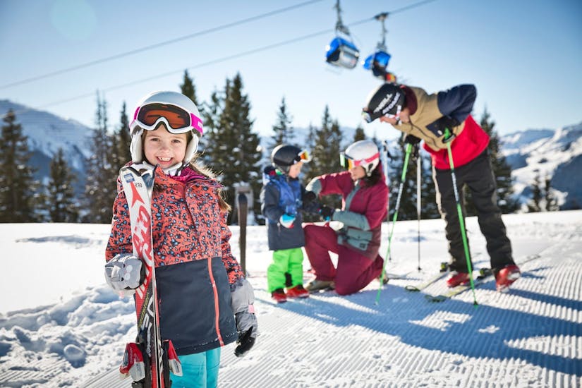 Two parents helping their kids get ready for their private ski lessons for kids of all ages with Snowacademy Saalbach.