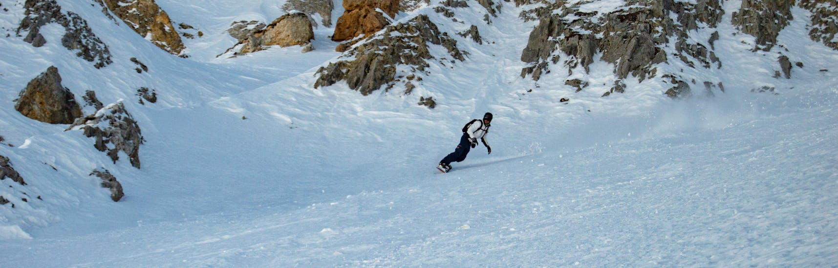 Un snowboarder está bajando la montaña durante sus clases particulares de snowboard (a partir de 8 años), para todos los niveles, con Evolution 2 Tignes.