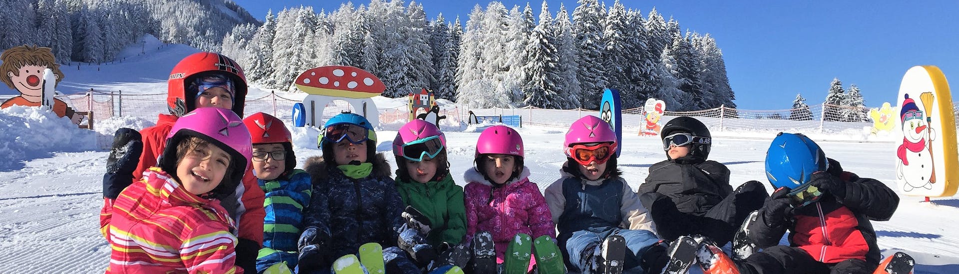 Kinder sitzen im Schnee während des Skikurses im "Junior Club" der Skischule Toblach.