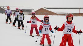 A group of kids skiing in a line during their Kids Ski Lessons “Kids Club” (4-16 y.) for Beginners from Ski School Ski Total Kirchdorf.