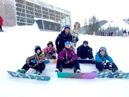 Children sit in the snow with their snowboards during their private snowboarding lessons for children & adults with the ski school Zell am See Outdo .