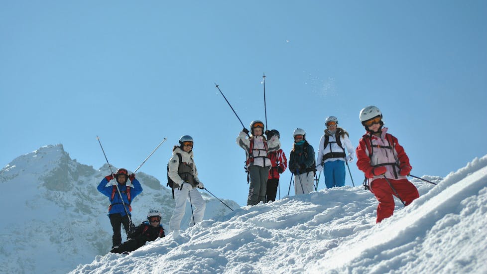 Een groep kinderen staat op de berg en zwaait met hun skistokken tijdens de skilessen "BOBOs Kinderclub" voor kinderen (4-14 jaar) van de skischool Fieberbrunn Widmann Mountain Sports.