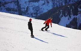 Een snowboarder volgt de instructeur van de skischool Red Carpet Champéry op een besneeuwde helling tijdens hun privélessen snowboarden - alle niveaus en leeftijden.