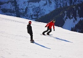 Un snowboardeur suit son moniteur de snowboard de l'école de ski Red Carpet Champéry le long d'une piste enneigée pendant son Cours particulier de snowboard - Tous niveaux & âges.