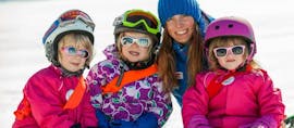 Drie kinderen met hun leraar lachen naar de camera tijdens hun skilessen voor kinderen "Bambini" voor beginners bij skischool Wilder Kaiser in St. Johann.