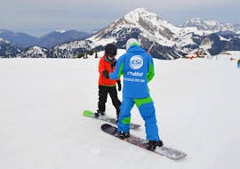 Un moniteur aide son élève à rester en équilibre sur son snowboard pendant un cours particulier de snowboard à Châtel avec l'ESI Pro skiing.