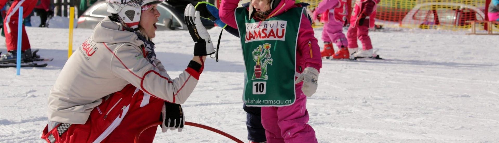 Een skileraar geeft een kind een high-five tijdens de skilessen voor kinderen "Bambini" voor alle niveaus bij skischool Ramsau.