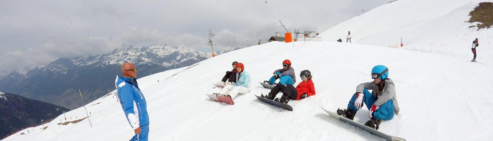 Tieners zitten in de sneeuw en luisteren naar hun snowboardleraar tijdens hun Skilessen voor Tieners (vanaf 13 jaar) - Gevorderden bij de skischool ESI Valfréjus.