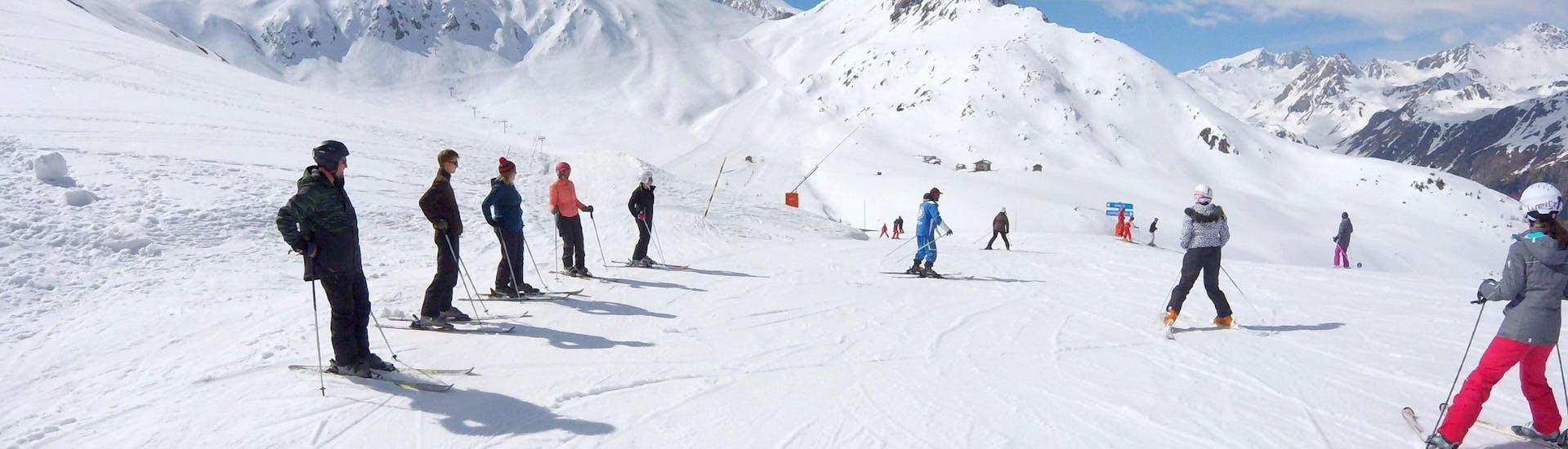 Een groep skiërs staat in het midden van een piste te wachten op de instructies van hun skileraar van de skischool ESI Valfréjus tijdens hun Skilessen voor Tieners & Volwassenen - Alle niveaus.