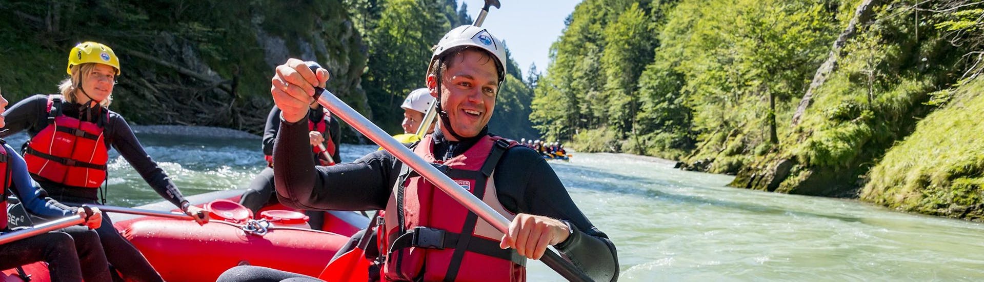 Ein Teilnehmer des Action Rafting auf der Tiroler Großache mit dem Adventure Club Kaiserwinkl Kössen paddelt in einem Raft durch eine spritzige Stromschnelle.