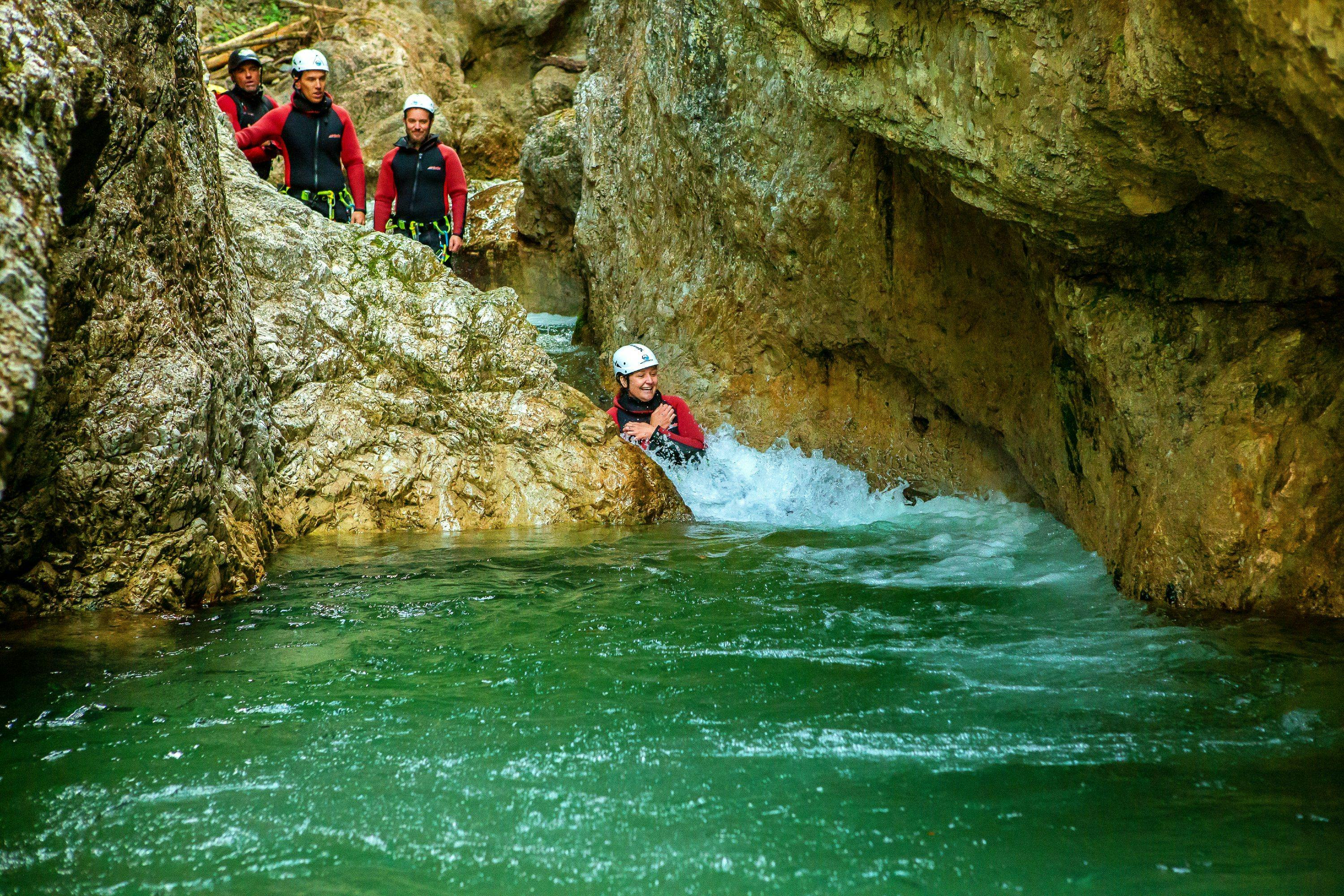 Outdoor-Kombi mit Rafting & Canyoning in Kössen Eine Frau, die bei ihrer Outdoor-Kombi Rafting & Canyoning mit dem erfahrenen Team von Adventure Club Kaiserwinkl in ein Naturbecken hineinrutscht.