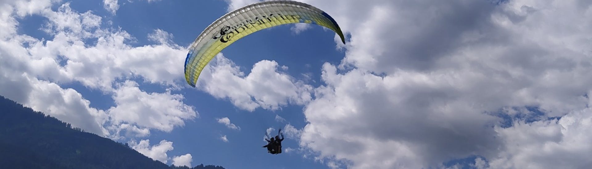 Een deelnemer en een instructeur vliegen boven de grond vlak voor de landing tijdens tandem paragliden Zillertal in Hintertux - thermische vlucht met Fly 2095 Zillertal.