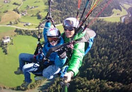 A child and instructor flying through the air during Tandem Paragliding from Unterberghorn for Kids (up to 14 y.) Airtaxi Kössen.