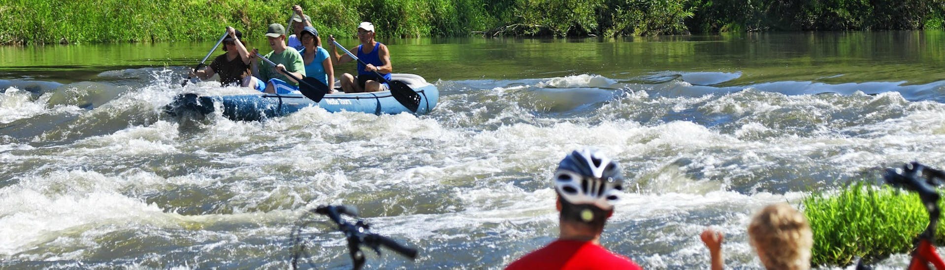 Zwei Fahrradfahrer beobachten das Raftingboot im Fluss bei der Rafting- & Fahrradtour auf der Neiße mit Neisse Tours Rothenburg