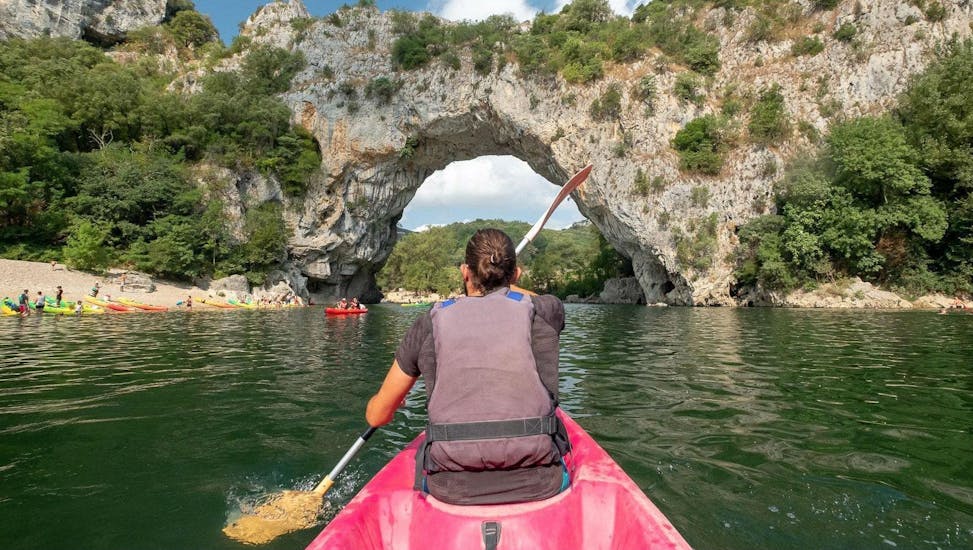 Durante il tour "Maxi-Discovery 13km" in Ardèche, una coppia passa sotto il famoso arco del Pont d'Arc mentre è seduta in una canoa di alta qualità affittata ad Aigue Vive.
